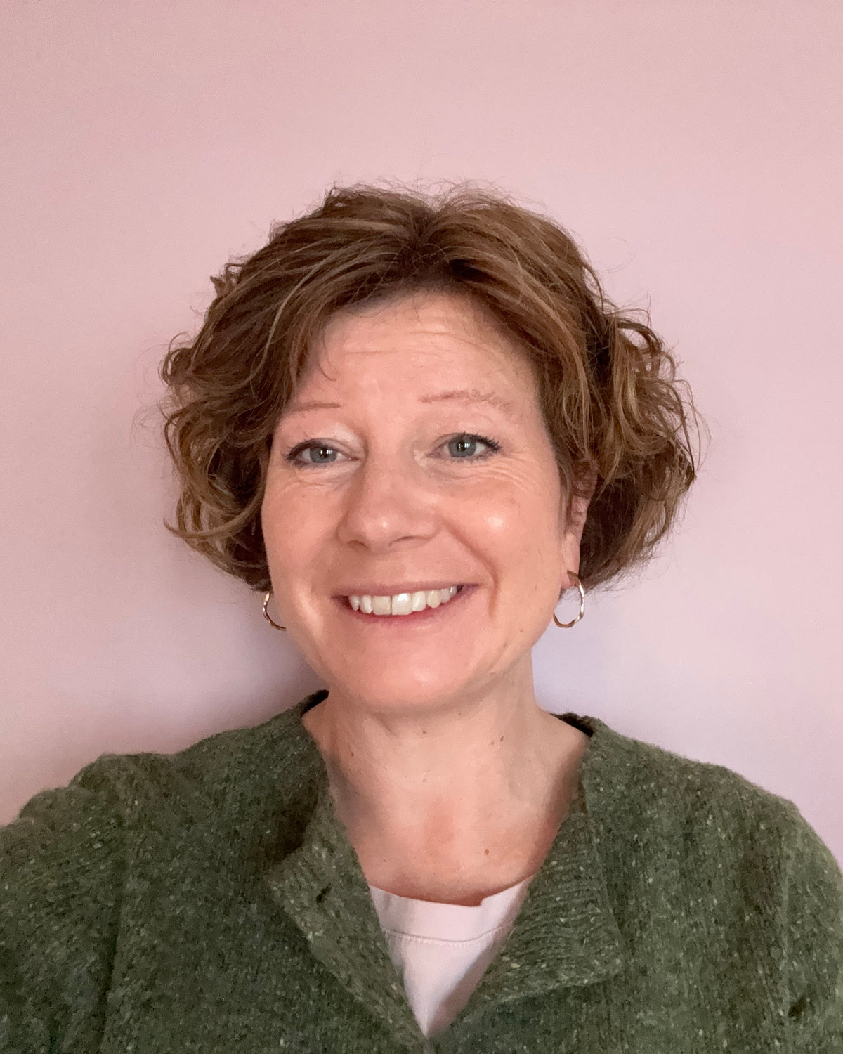 Person wearing a green cardigan on a pink background